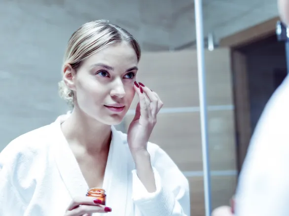 Young woman with red nails taking care of her skin on face