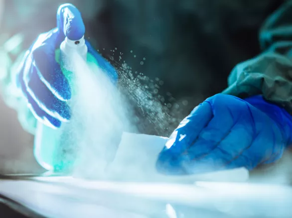 Healthcare professional sanitizing a surface by spraying disinfectant and wiping it