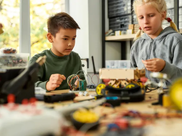 Asian boy and caucasian girl making their own vehicles at a stem robotics class. Inventions and creativity for children. Science and people concept.