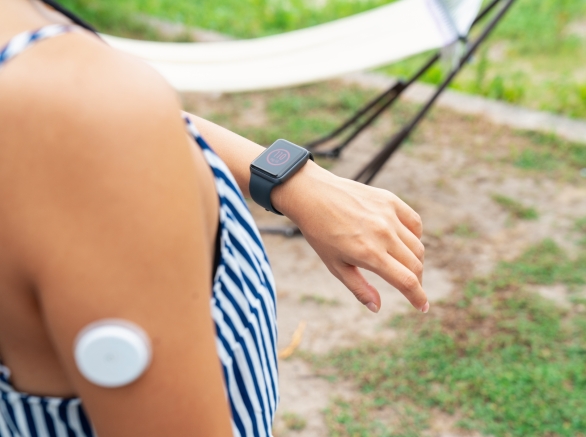 A person wearing a medical device on their arm, while checking their smart watch
