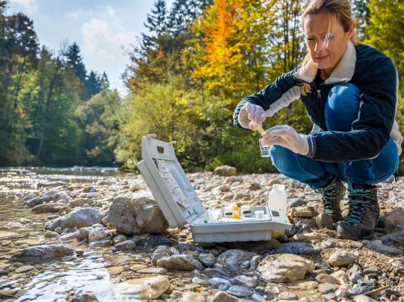 Mature female biologist adding reagent into a vial with water sample near river.