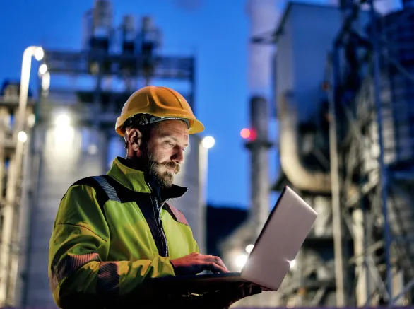 Young engineer wearing a helmet and using a laptop during his night shift. Engineering concept.