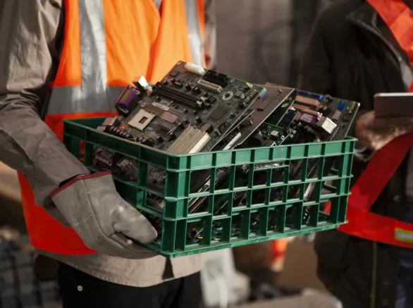 Portrait of female and male recycling coworkers holding digital tablet and plastic box full of old mother boards while looking at the camera