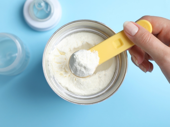 Woman Taking Powdered Infant Formula With Scoop From Can On Light Blue Background