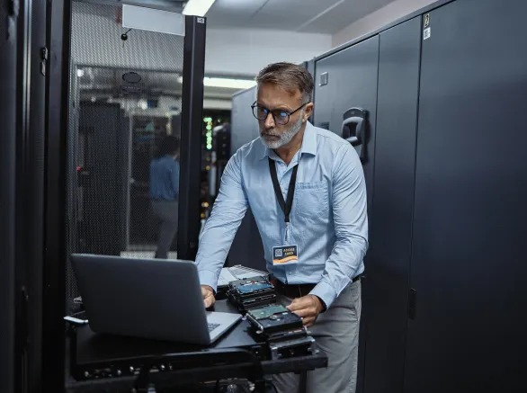 Mature software engineer using a laptop in a server room. IT technician working on network programming with online technology. Protecting information on the internet with cyber security management