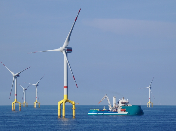 A windfarm in a body of water with a ship sailing nearby