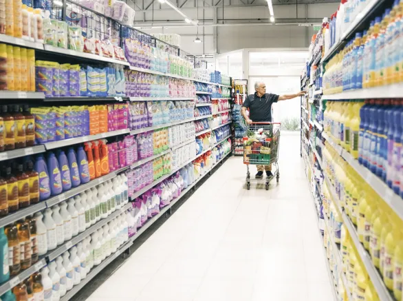 Senior man with shopping cart in supermarket aisle. Mature male customer looking at groceries in store.