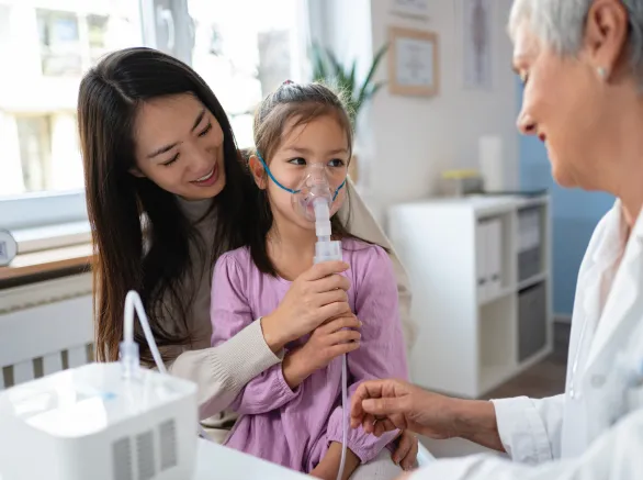 In the ordination, while sitting in her mother lap, Japanese girl receiving a treatment with nebulizer, from the senior Caucasian female pediatrician