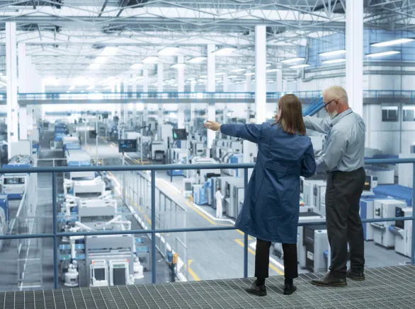 Experienced Male and Female Engineers Standing on a Platform with Their Back to Camera, Using Laptop Computer and Discussing Production at a Modern AI Automated Electronics Manufacture