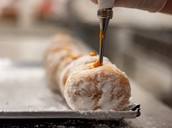 Close-up on a baker filling donuts with a caramel sauce at an industrial bakery - business concepts