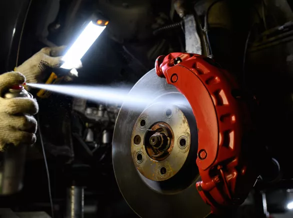 Car mechanic in gloves holding lamp and spraying disc brake fluid in garage