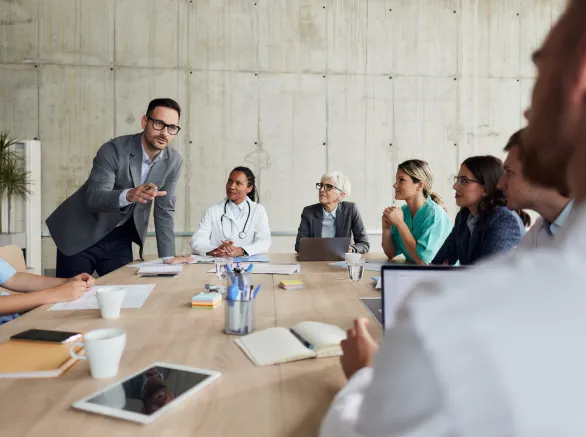 Male administrator talking during a meeting with his colleagues and group of doctors in hospital. Copy space.
