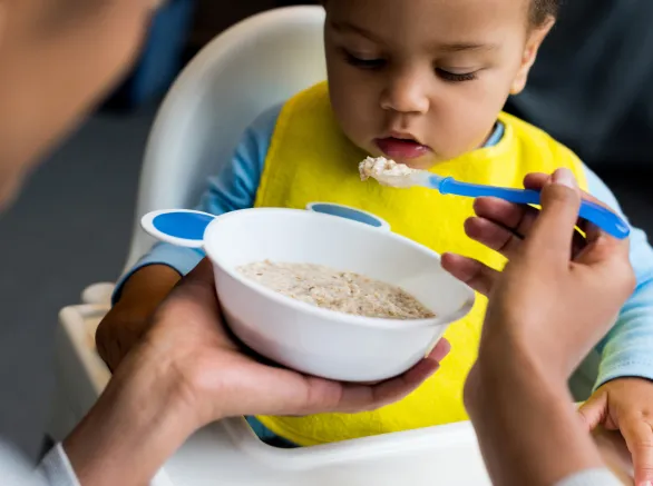 african american mother feeding little son with porridge at home