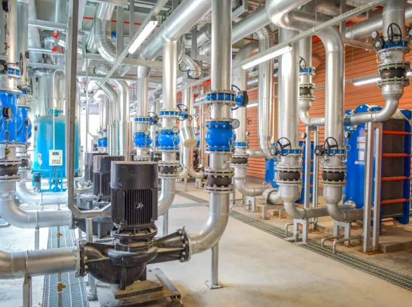 Inside view of process plant and equipment with large pipes and tubes running from floor to ceiling and across the ceiling