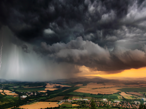Aerial view of dark brooding storm clouds with lightening passing over urban development and open fields