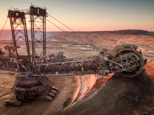 Crane-like machine excavating the earth, glowing red from sunlight, in the middle of a dirt plateau