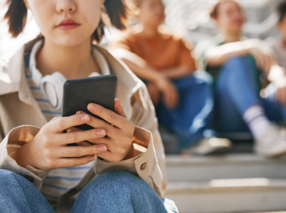 Young woman with headphones around her neck looking at her cell phone screen while sitting in the bleachers with a row of young people sitting in the background