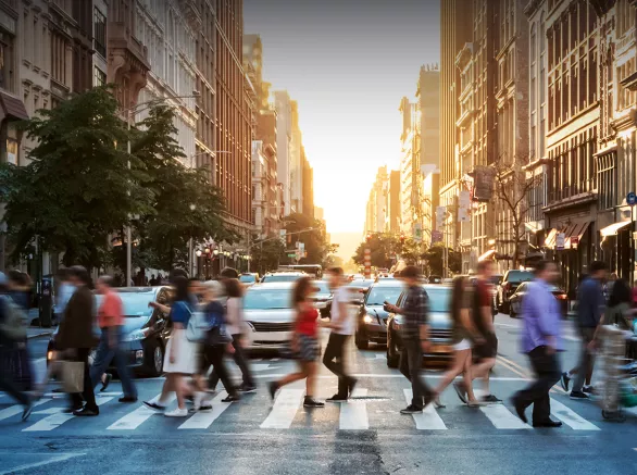 A crowd of people use a cross walk in a large city. Exponent helps build more inclusive technologies for all.
