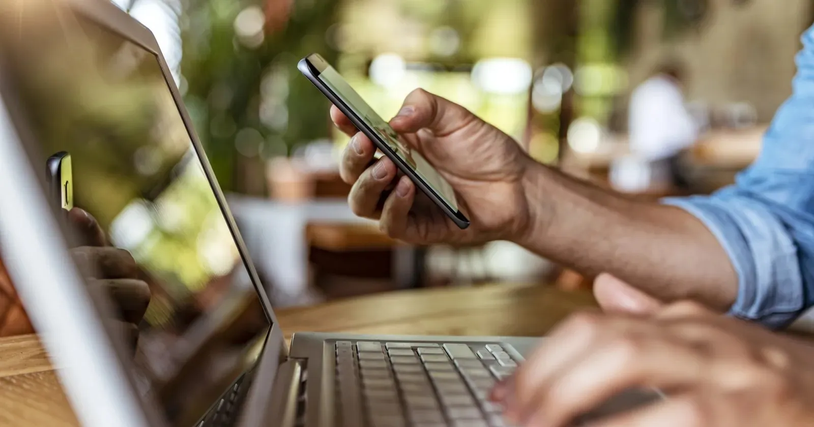 Man holds phone and uses laptop. 