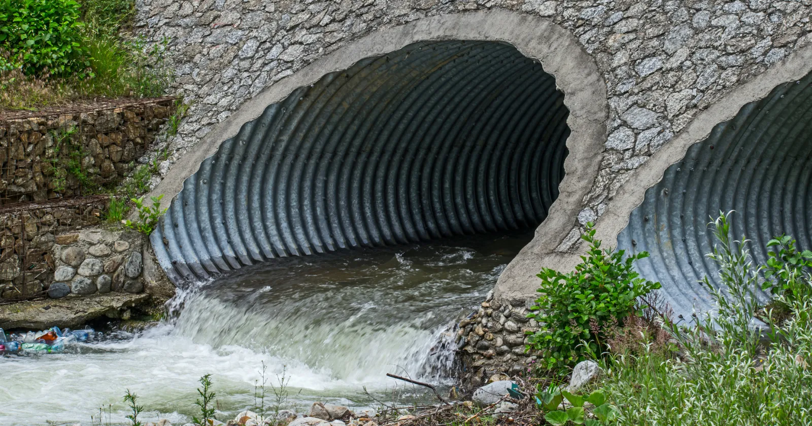 Water drains through pipes, under a bridge.