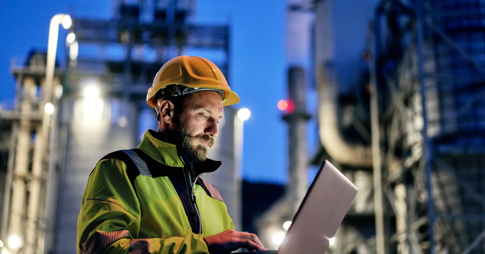 Young engineer wearing a helmet and using a laptop during his night shift. Engineering concept.