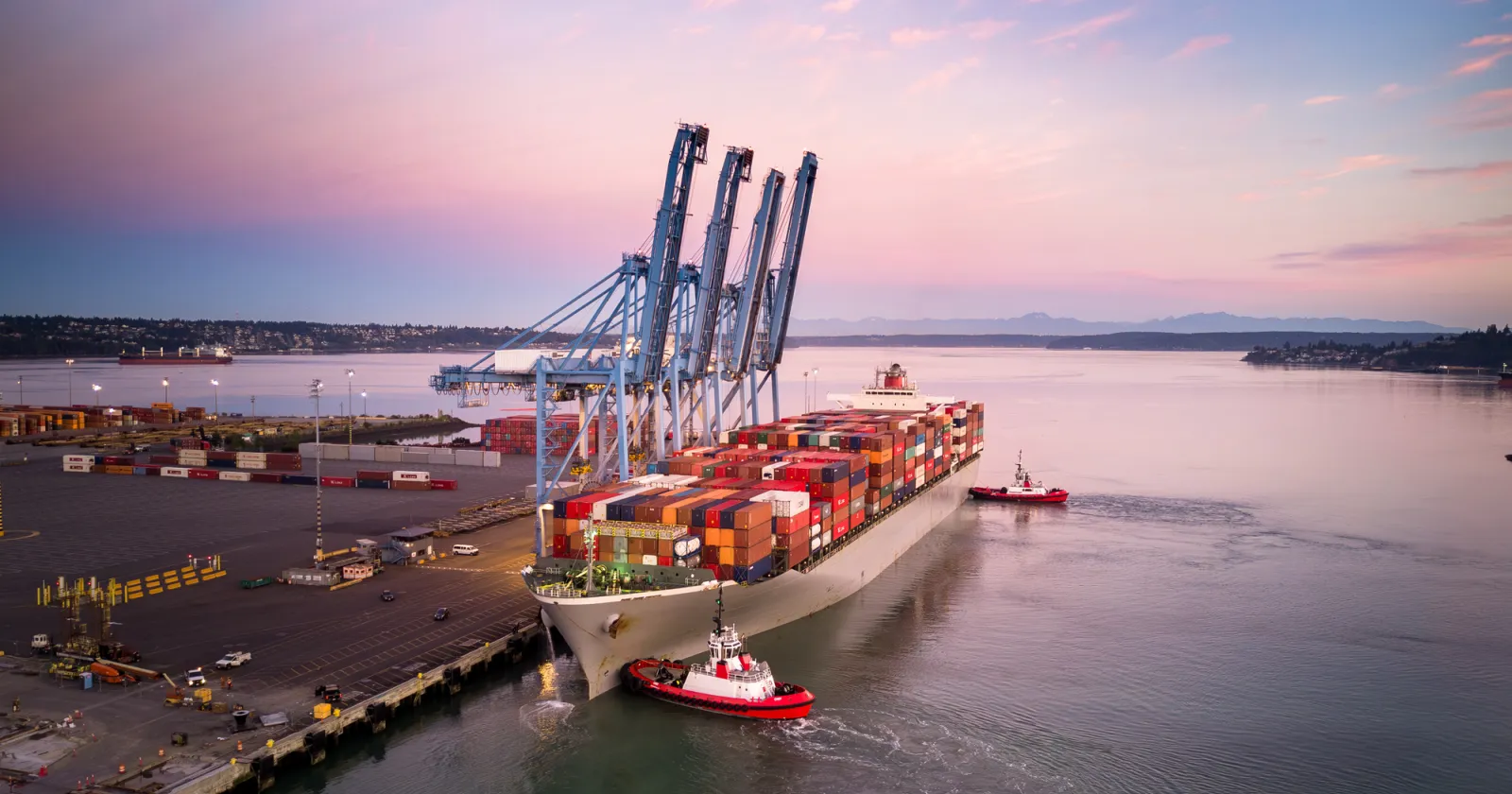 A high angle still image of a cargo ship with numerous containers on Blair Waterway, parked on container terminal in the Port of Tacoma, Washington at sunrise.