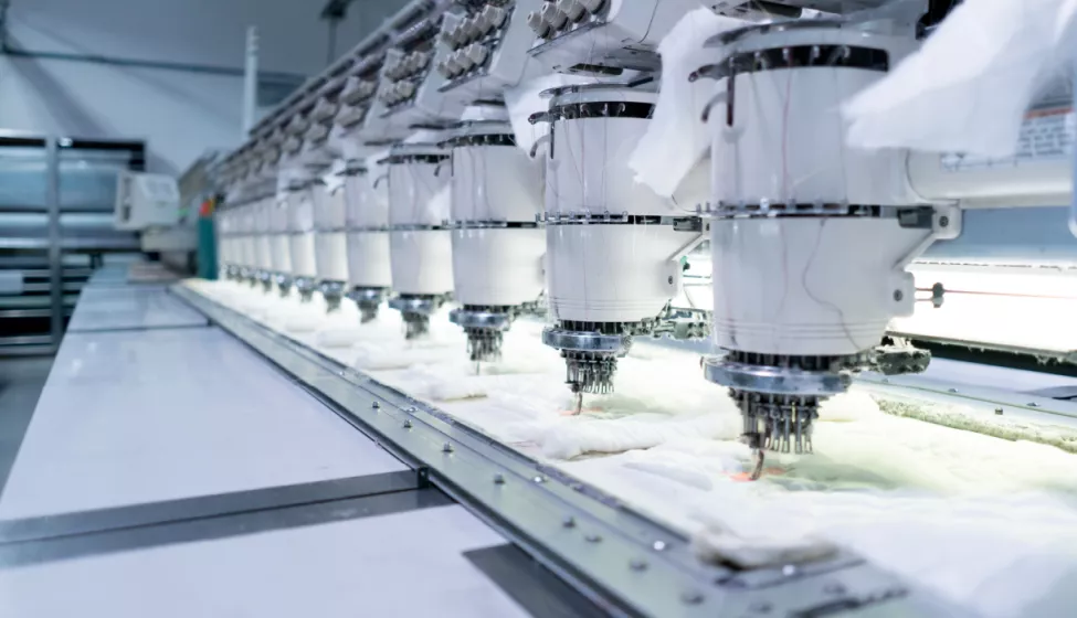 An embroidery machine with a row of multiple units simultaneously embroidering clothing 
