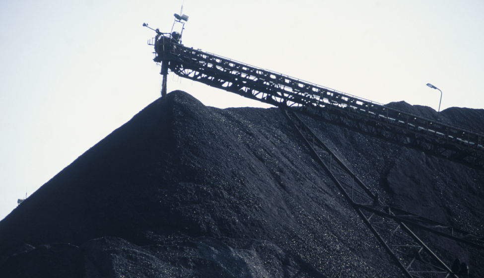 Huge mounds of black coal with crane hovering over top of mound