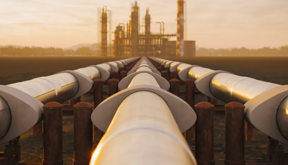 Three pipelines extending over a field with a refinery in the background