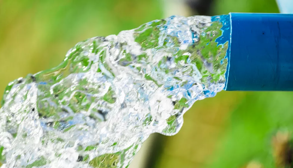 Close-up of water flowing out of a blue hose against green-blue background