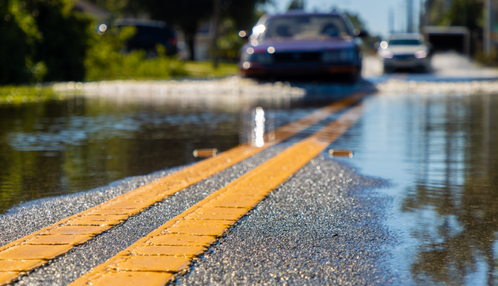 Two cars driving on a flooded road with a close-up of the yellow dividing lines