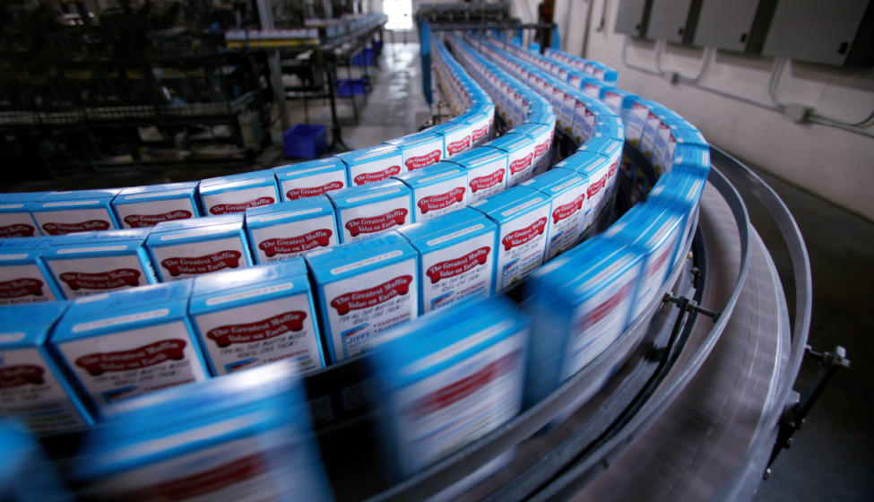 5 rows of blue-trimmed muffin mix boxes whizzing by on an assembly-line manufacturing plant