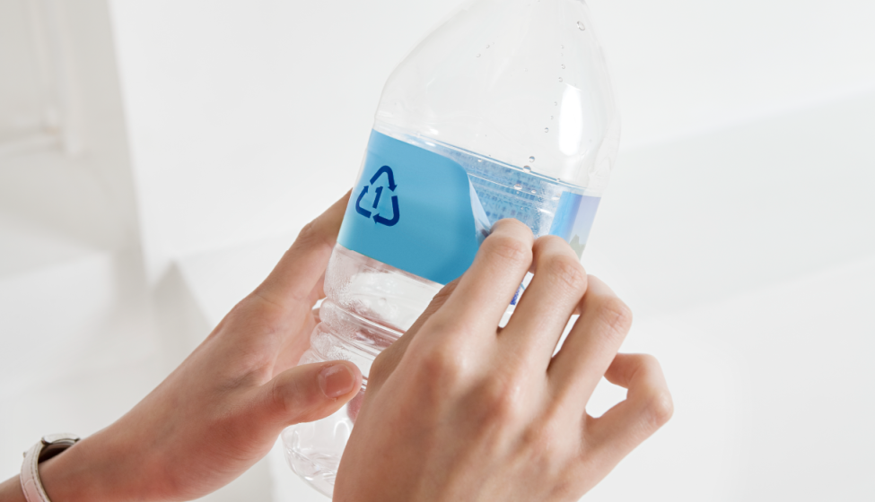 Two hands holding up small water bottle with blue label and recycling (chasing arrows) triangle symbol against a white background