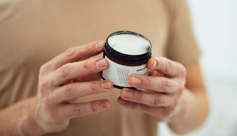 Person holding a cosmetic cream container reading the label on the back