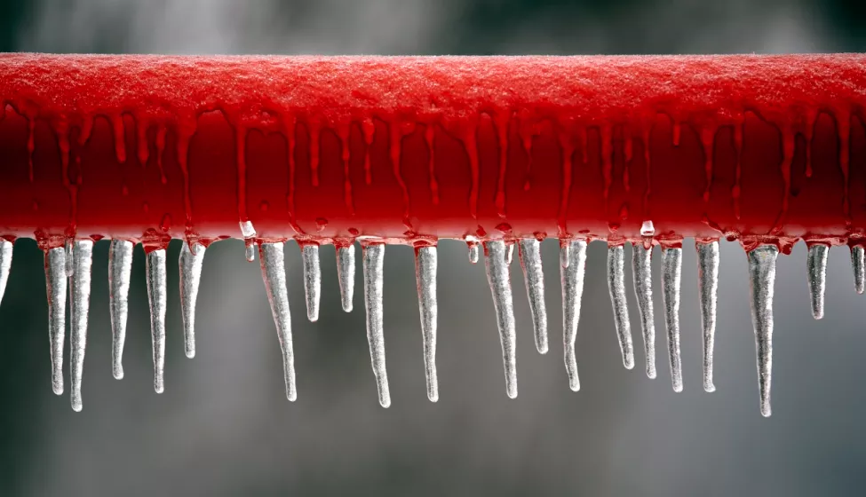Close up of a horizontal red pipe that is frozen with icicles hanging from it 