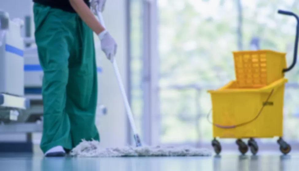 A healthcare worker in green scrubs mops the floor, with mopping bucket in foreground