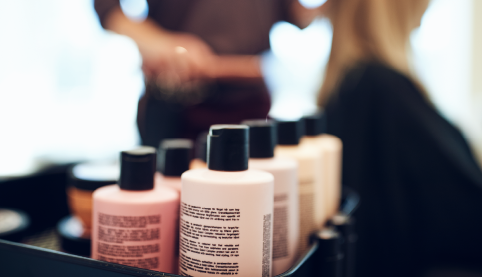 Close up of bottles of hair dye on a cart in a salon with a hairstylist working on a client in the background out of focus