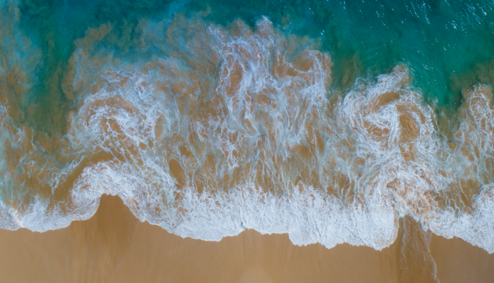 Bird's eye view of an ocean wave hitting a sandy beach