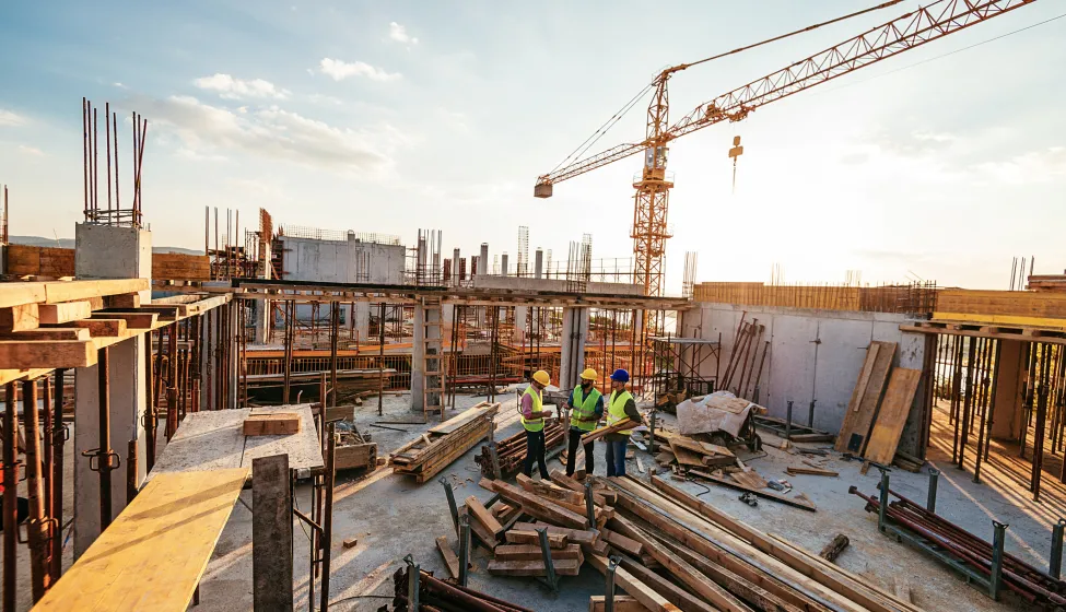 Construction industry concept - architects and engineers discussing work progress between concrete walls, scaffolds and cranes.