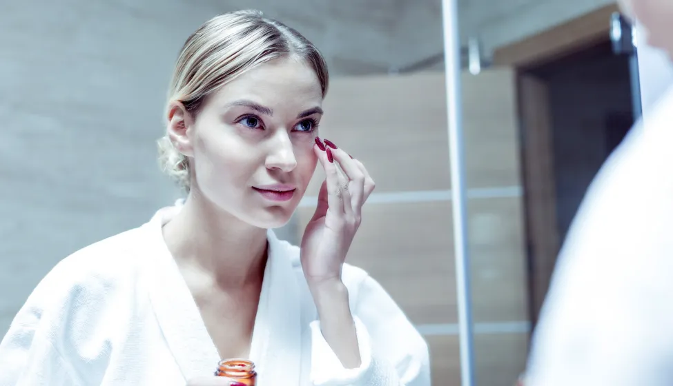 Young woman with red nails taking care of her skin on face