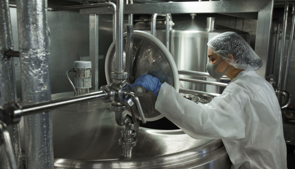 An industrial food factory worker opens a stainless steel vat. Exponent helps food and beverage manufacturers improve food safety.