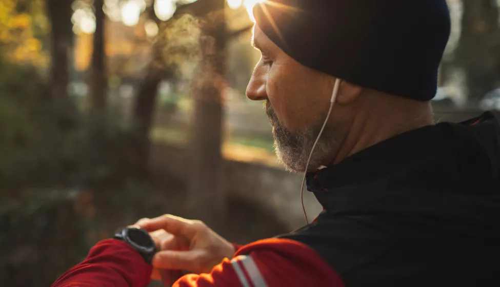 A man on checking his smart watch while on a run through a trail.