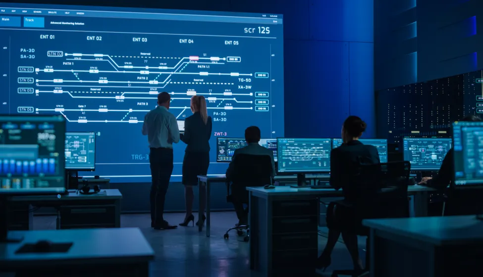 Telecommunications Company System Control and Monitoring Room with Diverse Multicultural Team of Professionals Working on Computers. Big Screen Display Showing Infrastructure Infographics. Back View