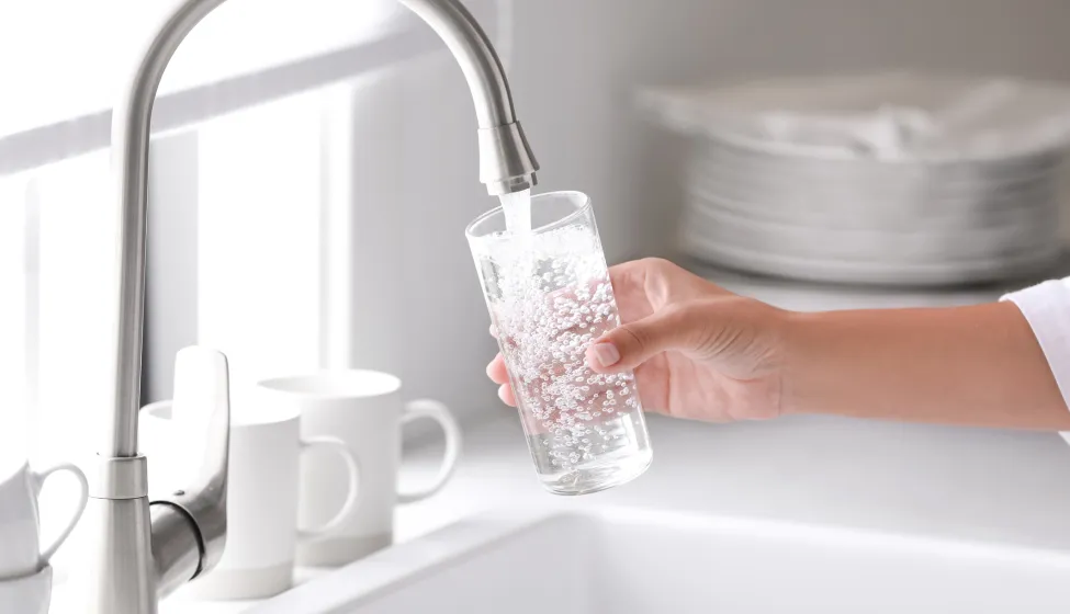 Woman pouring water into glass in kitchen, closeup