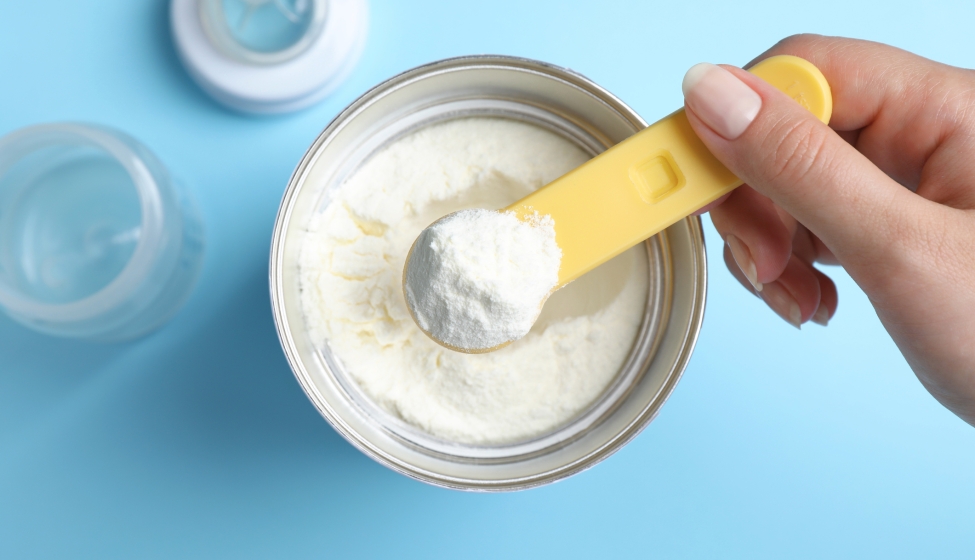 Woman Taking Powdered Infant Formula With Scoop From Can On Light Blue Background