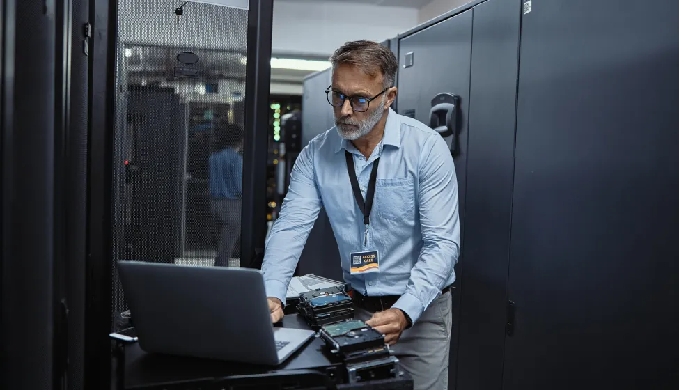 Mature software engineer using a laptop in a server room. IT technician working on network programming with online technology. Protecting information on the internet with cyber security management