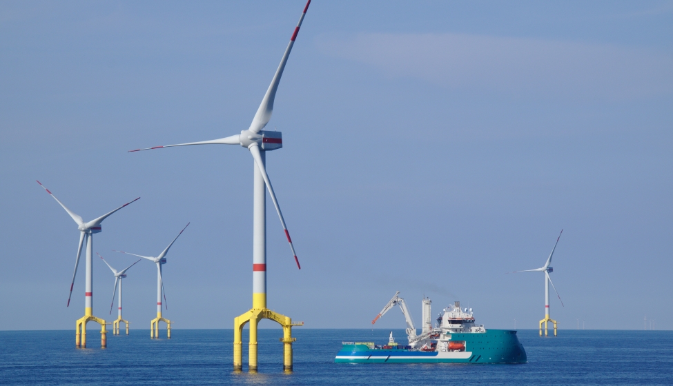 A windfarm in a body of water with a ship sailing nearby