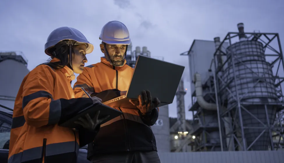 Man and woman working late with laptop in a power plant. Night shift.