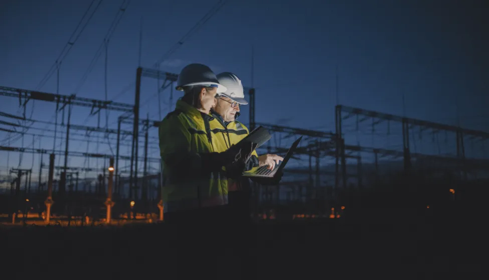 Electrical Engineers Discussing Over Laptop At Dark Power Plant During Night