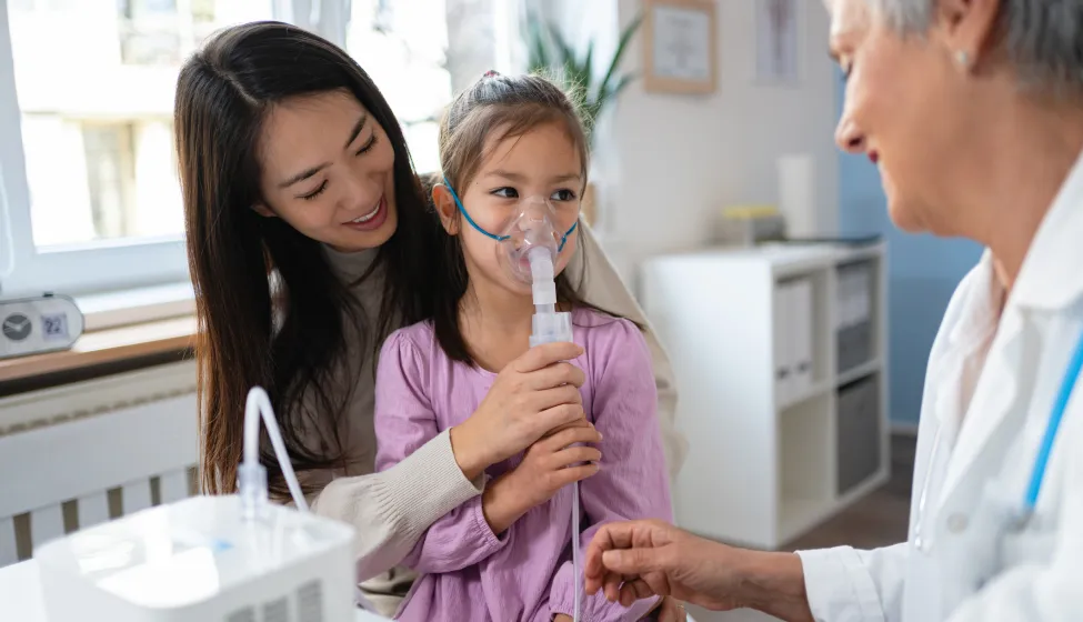 In the ordination, while sitting in her mother lap, Japanese girl receiving a treatment with nebulizer, from the senior Caucasian female pediatrician